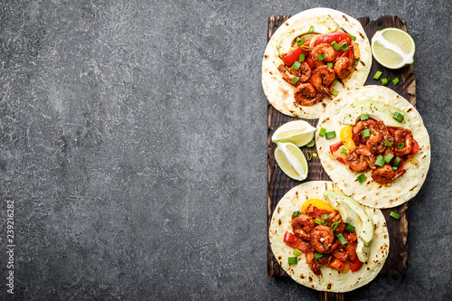 Fajitas in tortillas with fried shrimps, bell peppers and onion served up with avocado and green onions on wooden cutting board, top view, food background with space for a text