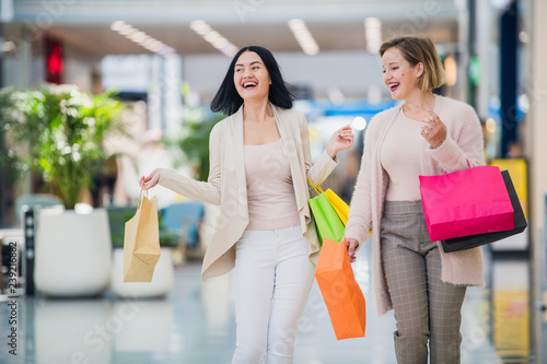 Laughing girls carrying bags with purchases in shopping mall
