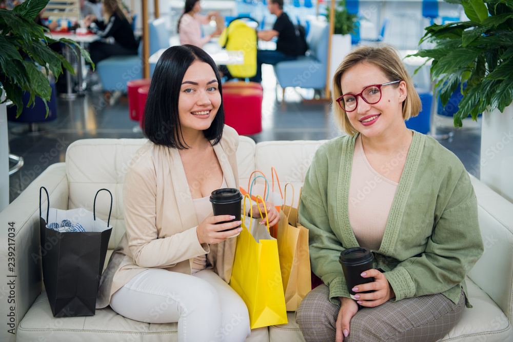 Portrait of smiling women with shopping bags and coffee to go looking at camera at the shopping mall