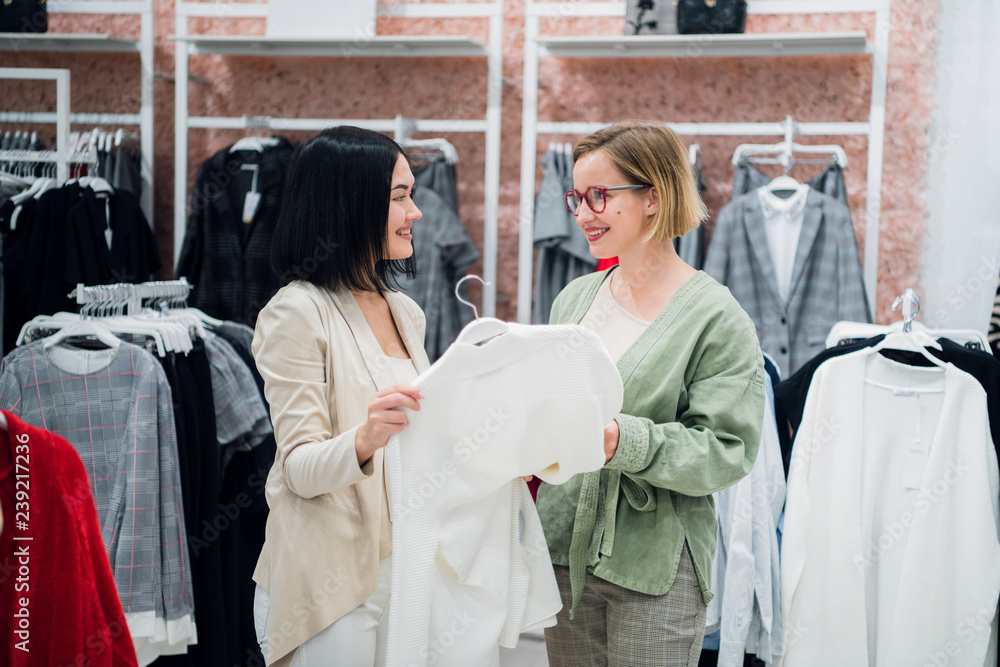 Beautiful girls are choosing clothes, talking and smiling while doing shopping in boutique Beautiful girls are choosing clothes, talking and smiling while doing shopping in boutique