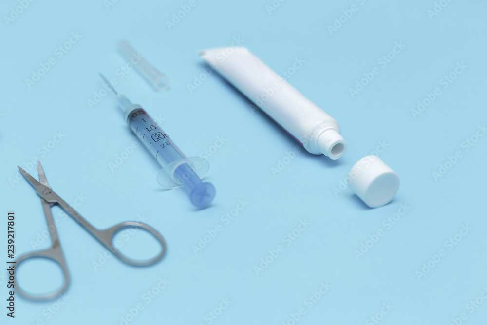 Tube of ointment, scissors and syringe on a blue background Tube of ointment, scissors and syringe on a blue background
