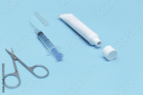 Tube of ointment, scissors and syringe on a blue background