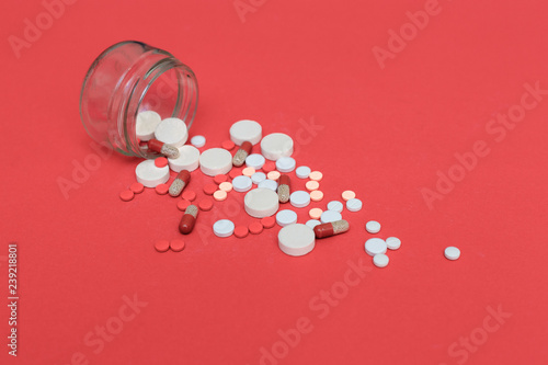 Different pills scattered from a flask on a red background