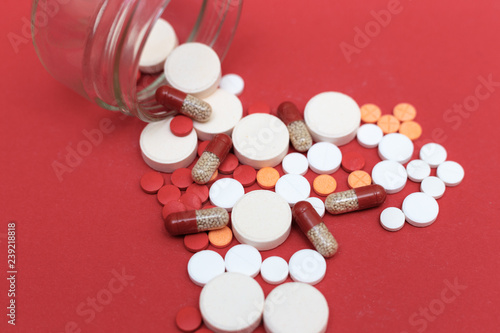 Different pills scattered from a flask on a red background closeup