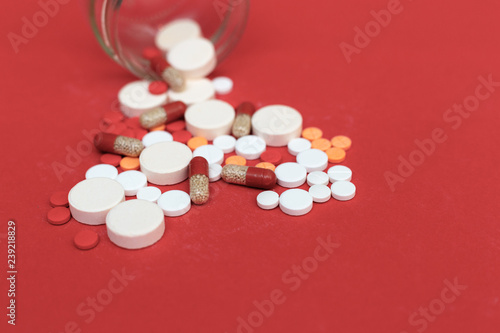 Pills scattered from a flask on a red background closeup
