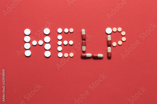 Pills scattered  on a red background closeup. Inscription help