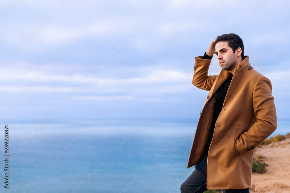 in a beige coat standing on the shore of the ocean and admiring in a beige coat standing on the shore of the ocean and admiring