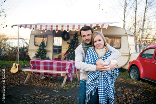 Beautiful young couple standing with hot coffee in the background of a camper van  in the autumn day.