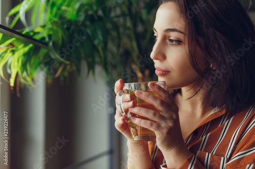 Woman sit on stairs at home, smell her green tea and feels great. Green tree on background and copy space fot text