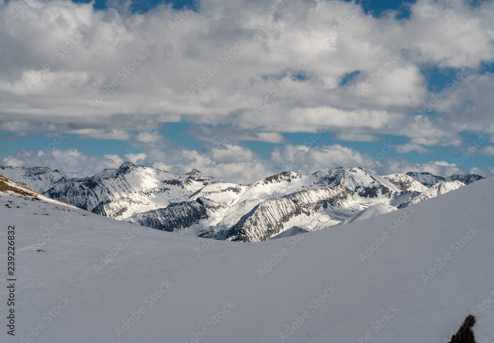 Snow covered Rocky Mountain ranges rise into while fluffy clouded skies