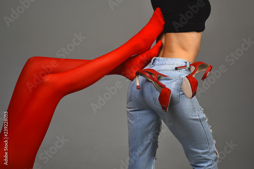 Slim woman body in blue torm jeans and black shirt with red heels on grey background. Legs in red stockings touch naked waist of another girls. Homosexual concept of two girls together. Lesbian life