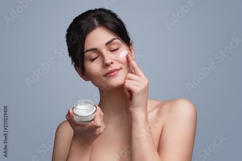 Happy woman applying soft cream on face
