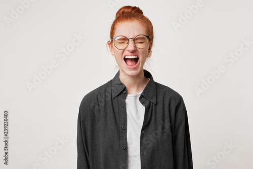 Yelling scared red-haired girl, looks frightened afraid, mouth wide openes as screaming shouting loud, eyes closed, over white background photo