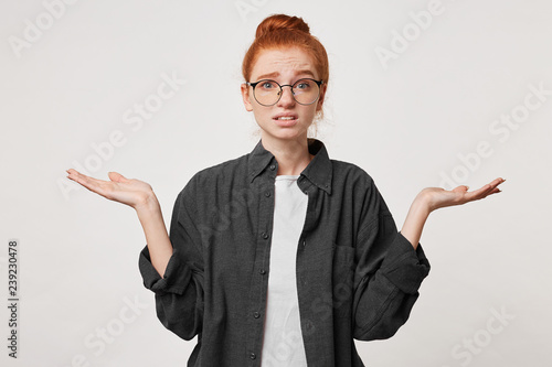Studio photo of a girl with red hair wearing glasses dressed in a man's black shirt depicts helplessness hopelessness holding hands to the sides with her palms upwards. Confused scared apologizes.