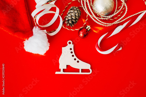 Wooden decoration on the Christmas tree in the form of a figure skate on a red background surrounded by Christmas elements. Place for text.