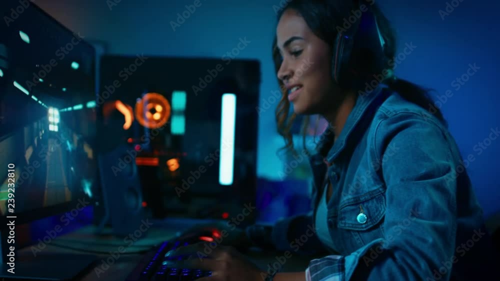 Pretty and Excited Black Gamer Girl Puts On Her Headset with a Mic and Starts Playing Shooter Online Video Game on Her Computer. Room and PC have Colorful Neon Led Lights. Cozy Evening at Home. Pretty and Excited Black Gamer Girl Puts On Her Headset with a Mic and Starts Playing Shooter Online Video Game on Her Computer. Room and PC have Colorful Neon Led Lights. Cozy Evening at Home.