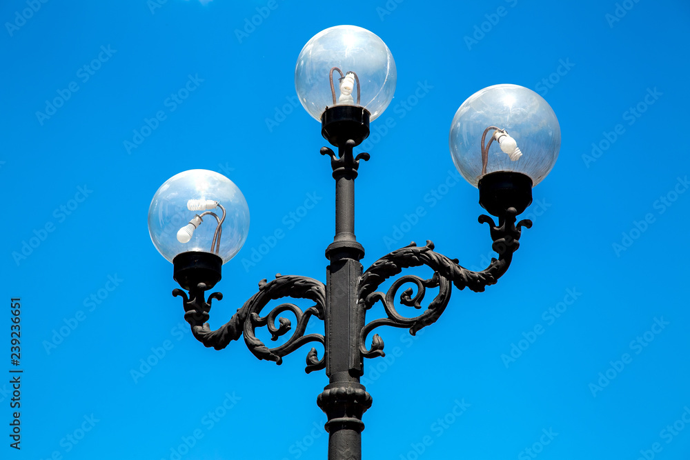 Lamppost with a triple lamp and round glass transparent shades against the blue sky. Lamppost with a triple lamp and round glass transparent shades against the blue sky.