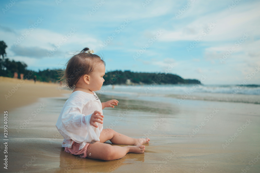 little girl in white clothes playing with sand on the beach among the waves little girl in white clothes playing with sand on the beach among the waves