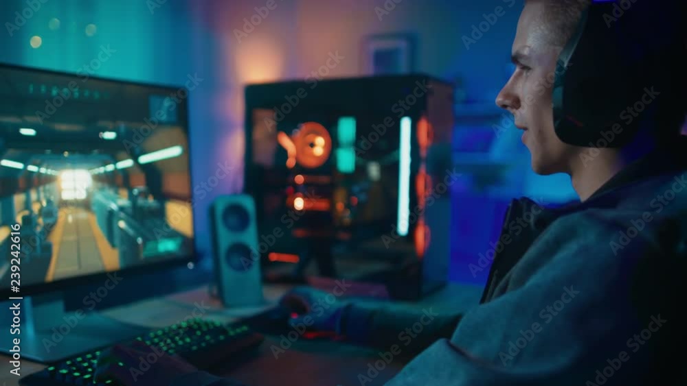 Happy Gamer in Headset with a Mic Playing Shooter Online Video Game on His Personal Computer. He Gives Commands to Other Players. Room and PC have Colorful Neon Led Lights. Cozy Evening at Home. Happy Gamer in Headset with a Mic Playing Shooter Online Video Game on His Personal Computer. He Gives Commands to Other Players. Room and PC have Colorful Neon Led Lights. Cozy Evening at Home.