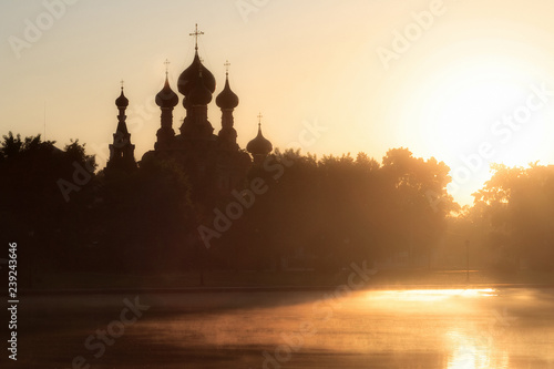 Beautiful sunny landscape with an old Russian orthodox church and a pond. Above the water in the sun rays is visible fog. Church of the Trinity in Ostankino, Moscow, Russia.