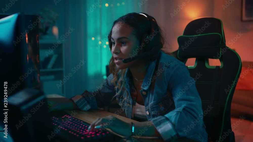 Excited Gamer Girl in Headset with a Mic Playing Online Video Game on Her Personal Computer. She Talks to Other Players. Room and PC have Colorful Warm Neon Led Lights. Cozy Evening at Home. Excited Gamer Girl in Headset with a Mic Playing Online Video Game on Her Personal Computer. She Talks to Other Players. Room and PC have Colorful Warm Neon Led Lights. Cozy Evening at Home.