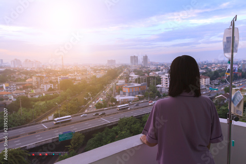 Patient wearing violet cloth need to go back home. Woman sickness standing on balcony of hospital room was homesick and looking at the sky in the direction of her home with sunset or sunrise