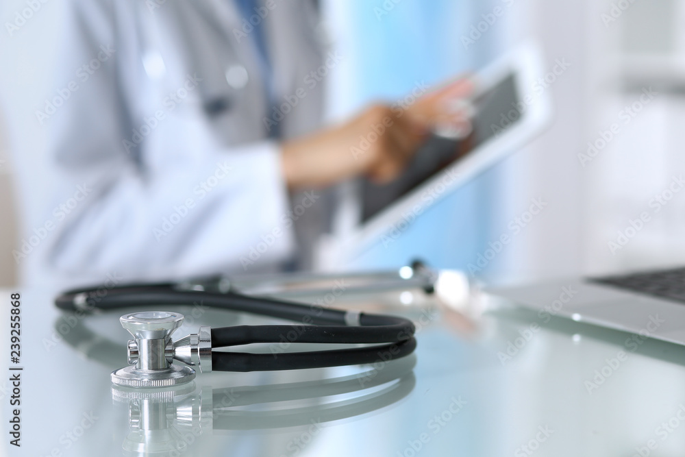 Stethoscope lying on glass desk with laptop computer at busy physician background. Medicine or pharmacy concept. Medical tools at doctor working table Stethoscope lying on glass desk with laptop computer at busy physician background. Medicine or pharmacy concept. Medical tools at doctor working table