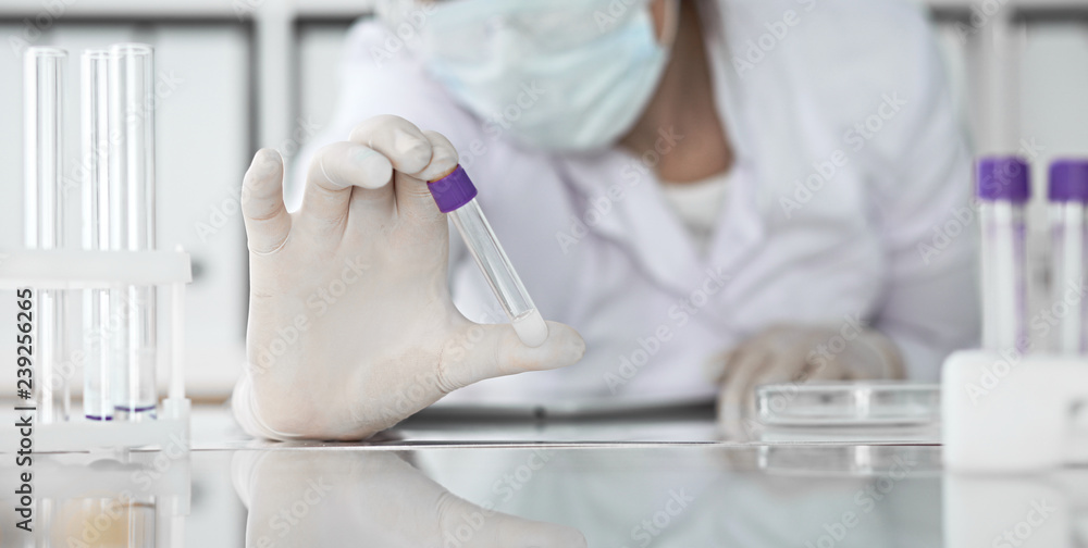 Close-up of professional female scientist in protective eyeglasses making experiment with reagents in laboratory or making blood tests. Medicine, science and research concept Close-up of professional female scientist in protective eyeglasses making experiment with reagents in laboratory or making blood tests. Medicine, science and research concept
