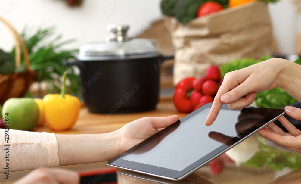 Close-up of human hands using tablet or touch pad. Two women in kitchen. Cooking, friendship or online shopping concepts Close-up of human hands using tablet or touch pad. Two women in kitchen. Cooking, friendship or online shopping concepts