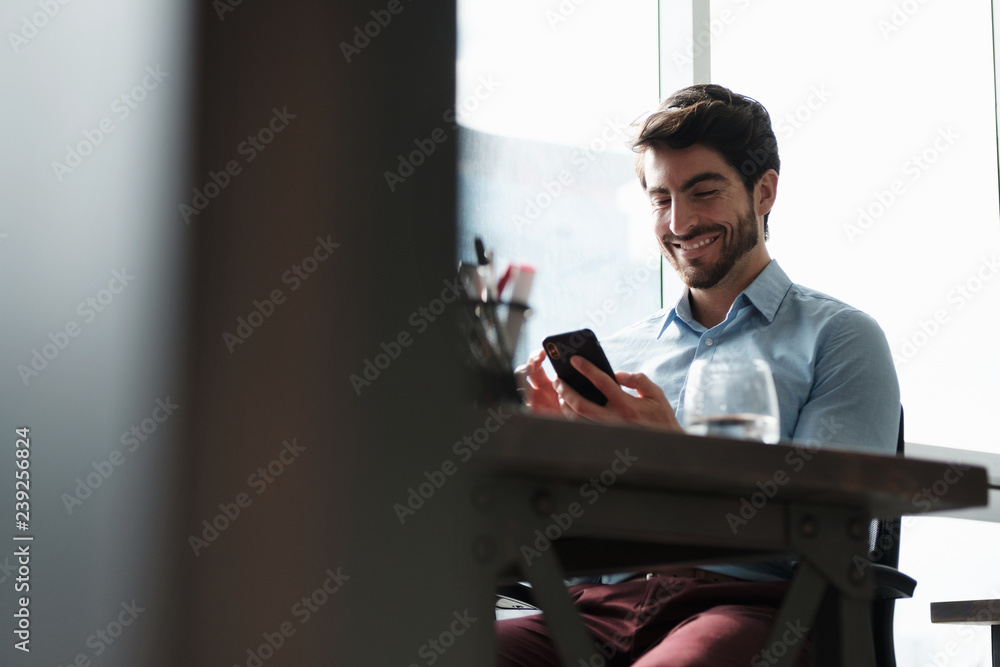 Fototapeta premium Man in Office Smiles After Sending Message Using Smartphone