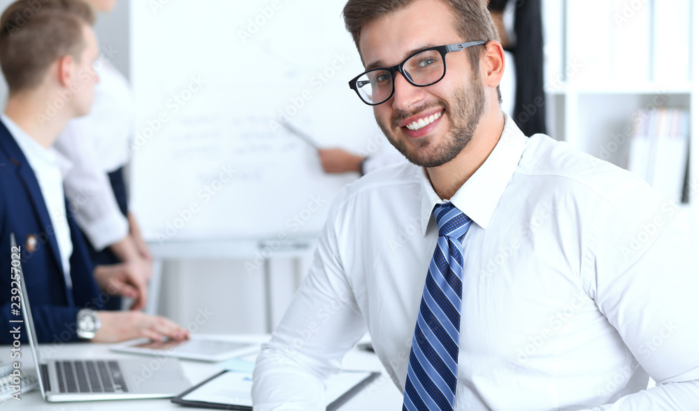 Fototapeta premium Business people at meeting in office. Focus at cheerful smiling bearded man wearing glasses. Conference, corporate training or brainstorming of people group. Success and negotiation concept