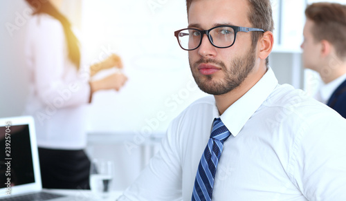 Business people at meeting in office. Focus at cheerful smiling bearded man wearing glasses. Conference, corporate training or brainstorming of people group. Success and negotiation concept photo