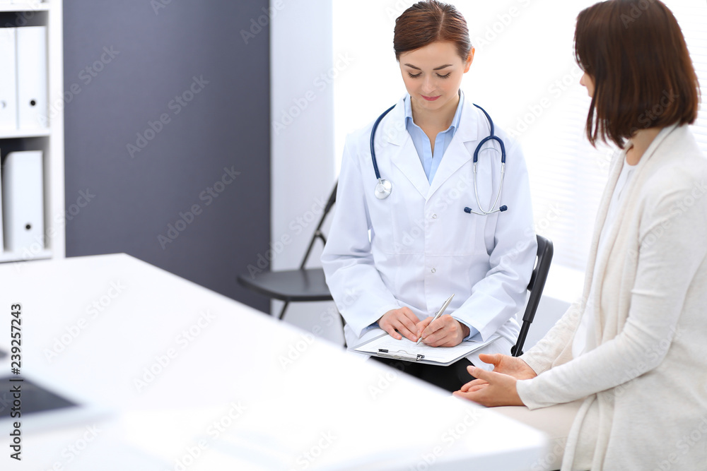 Happy doctor and patient discussing something while sitting at the chairs at hospital. Physician at work in clinic. Medicine and healthcare concept Happy doctor and patient discussing something while sitting at the chairs at hospital. Physician at work in clinic. Medicine and healthcare concept
