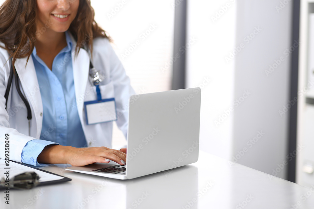 Unknown doctor woman typing on laptop computer while sitting at the desk in hospital office. close-up of hands. Physician at work. Medicine and health care concept Unknown doctor woman typing on laptop computer while sitting at the desk in hospital office. close-up of hands. Physician at work. Medicine and health care concept
