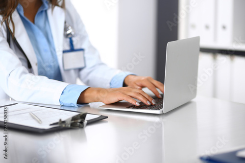 Unknown doctor woman typing on laptop computer while sitting at the desk in hospital office. close-up of hands. Physician at work. Medicine and health care concept