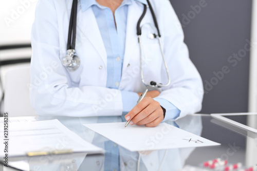 Doctor woman filling up prescription form while sitting at the desk in hospital close-up. Physician at work and ready to give an advice to help patient. Healthcare, insurance and excellent service i