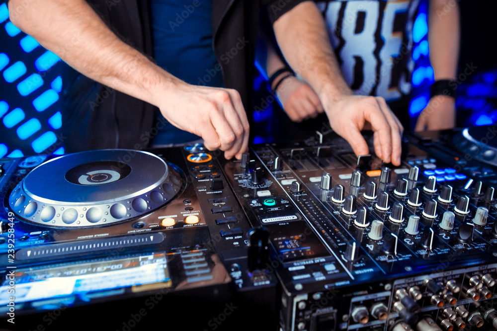 Naklejka premium Club party dj plays live set on stage in nightclub.Professional disc jockey mix popular musical tracks with vintage turnables & vinyl records