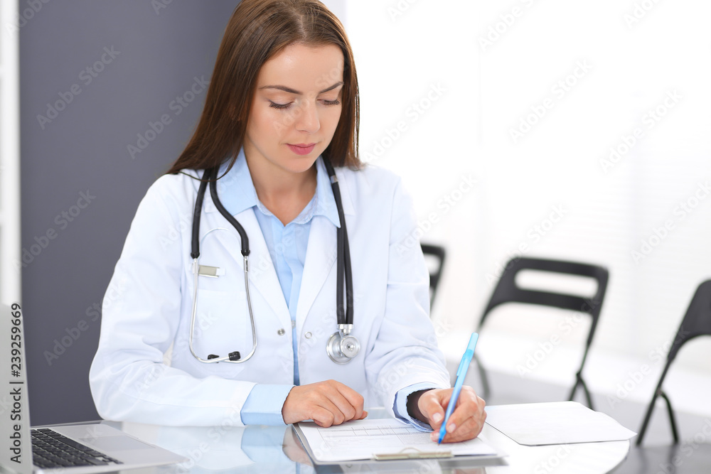 Doctor woman at work. Portrait of female physician filling up medical form while sitting at the glass desk at clinic or hospital. Medicine and healthcare concept Doctor woman at work. Portrait of female physician filling up medical form while sitting at the glass desk at clinic or hospital. Medicine and healthcare concept