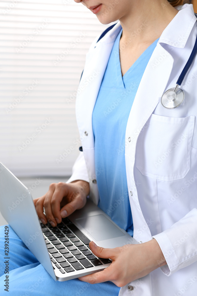 Woman doctor typing on laptop computer while working in hospital office, close-up. Data in medicine and health care Woman doctor typing on laptop computer while working in hospital office, close-up. Data in medicine and health care