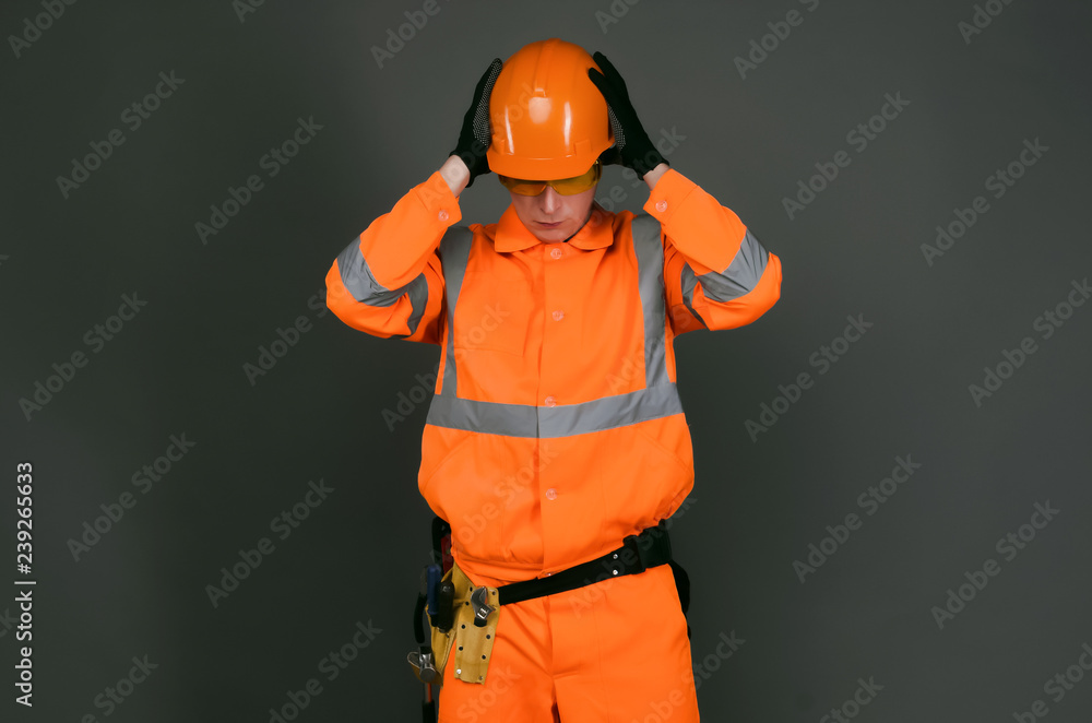 Tired and sad builder construction worker is holding a head by his hands isolated on gray background. Construction accident. Tired and sad builder construction worker is holding a head by his hands isolated on gray background. Construction accident.