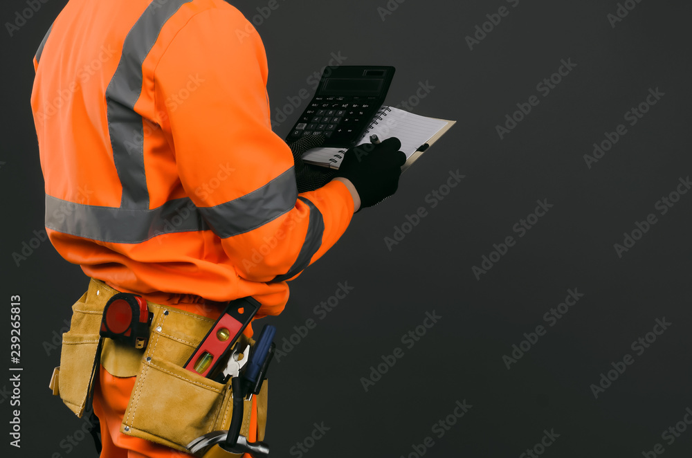 A construction worker with a calculator and a blank notebook in his hands. Cost calculation of repair or construction. A construction worker with a calculator and a blank notebook in his hands. Cost calculation of repair or construction.