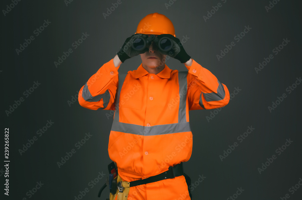 Geodesist or builder foreman is looking through a binoculars in his hands isolated on gray background.