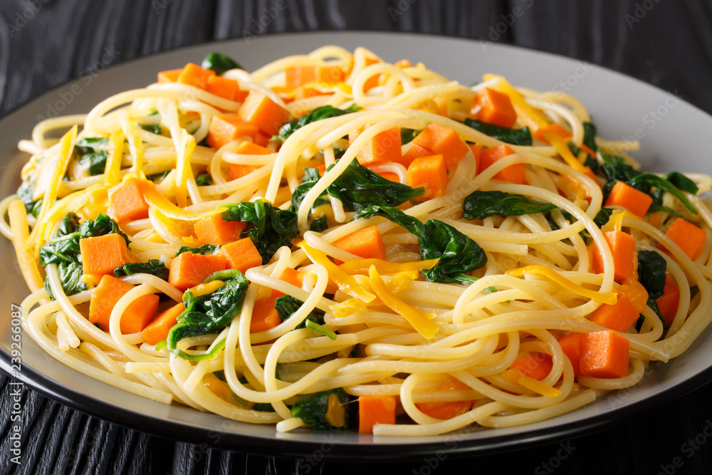 Healthy autumn meal of spaghetti with pumpkin, spinach and cheddar cheese close-up on a plate on the table. horizontal Healthy autumn meal of spaghetti with pumpkin, spinach and cheddar cheese close-up on a plate on the table. horizontal