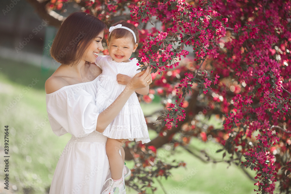 Portrait of young beautiful mother with her little baby girl. Close up still of loving family. Attractive woman holding her child in pink flowers and smiling. Portrait of young beautiful mother with her little baby girl. Close up still of loving family. Attractive woman holding her child in pink flowers and smiling.
