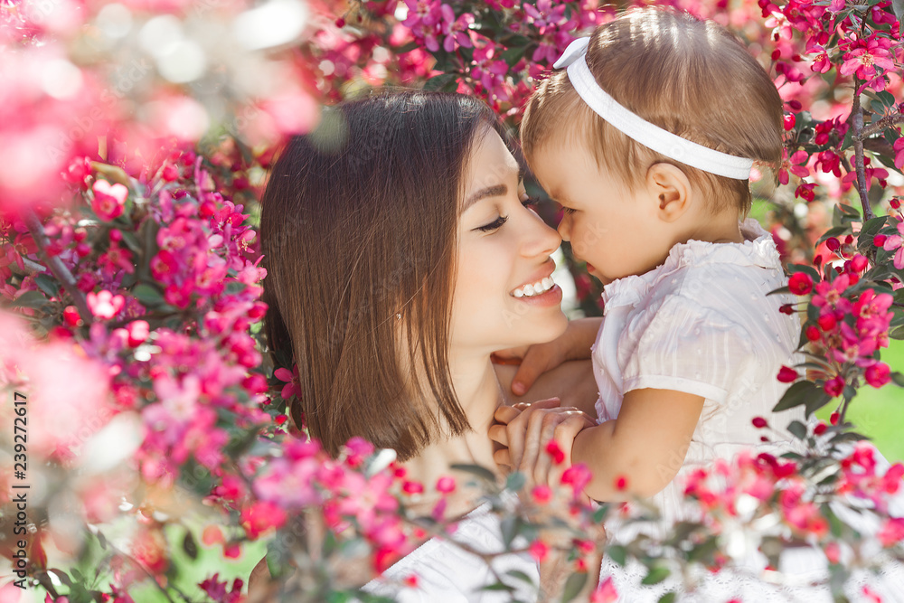 Portrait of young beautiful mother with her little baby girl. Close up still of loving family. Attractive woman holding her child in pink flowers and smiling. Portrait of young beautiful mother with her little baby girl. Close up still of loving family. Attractive woman holding her child in pink flowers and smiling.