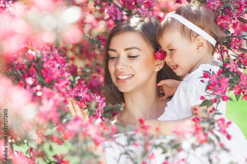Portrait of young beautiful mother with her little baby girl. Close up still of loving family. Attractive woman holding her child in pink flowers and smiling.