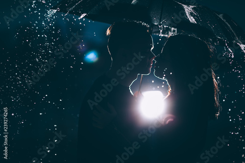 young couple standing under a dark umbrella photo