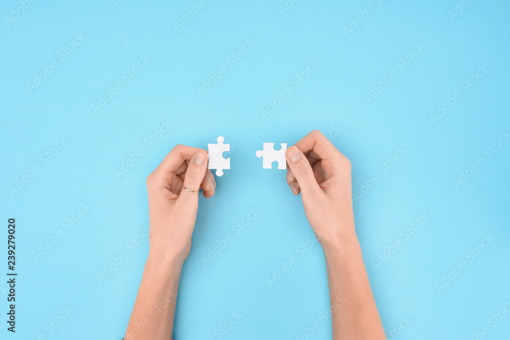 cropped shot of woman holding white puzzles pieces on blue background cropped shot of woman holding white puzzles pieces on blue background