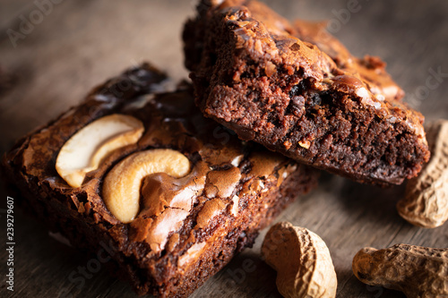 Brownie two slice with topping Cashew Nut and peanuts placed beside it. They are putting on a wooden desk.