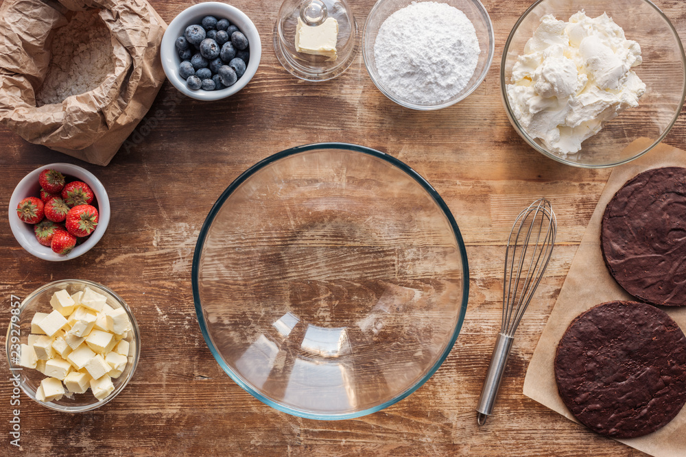 top view of empty glass bowl, whisk and ingredients for delicious homemade cake on wooden table top view of empty glass bowl, whisk and ingredients for delicious homemade cake on wooden table